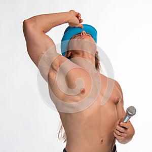 Singer bodybuilder shirtless with long hair in a blue hat with a microphone