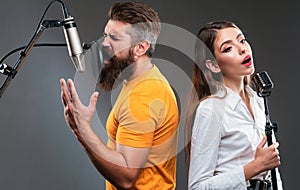 Singer duet couple is performing a song with a microphone while recording in a music studio.