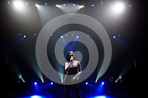 Singer perform on stage of nightclub in front of bright screen. Dark background, smoke, concert spotlights