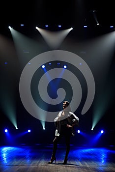 Singer perform on stage of nightclub in front of bright screen. Dark background, smoke, concert spotlights