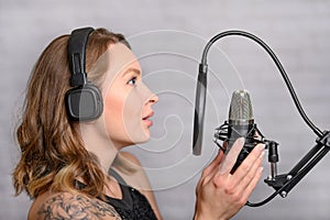 Singer with a tattoo sings rock music in the studio into a microphone, musician and treble vocals