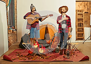 Singing anthem. Two men imagining, recreating camping activity indoors with necessary equipment. Concept of quarantine