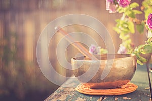 Singing bowl on a rustic wooden table with flowers, zen, outdoors