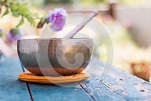Singing bowl on a rustic wooden table with flowers, zen, outdoors