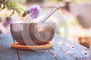 Singing bowl on a rustic wooden table with flowers, zen, outdoors