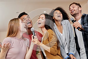 Singing for everyone. Cheerful multicultured friends singing with microphone while playing karaoke at home, standing