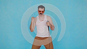 Singing funny young man with microphone in hand on blue background