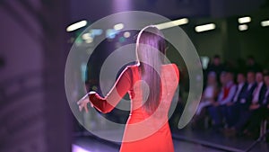 Singing girl artist in red dress on scene, Back view of girl singer in stage lights. Young woman singing song on live