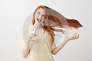 Singing her heart out. Portrait of cool confident emotive young woman with ginger hair that waves on air, holding