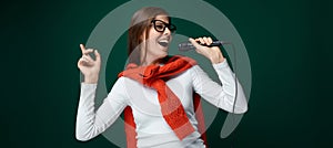 Singing young woman holding microphone on green background