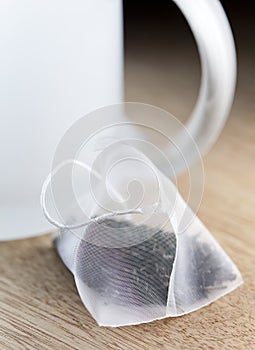 Single bag of elite tea in silk fabric packing and tea mug on a wooden background. Small depth of sharpness