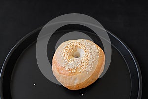 A Single Bagel with Sesame on dark plate