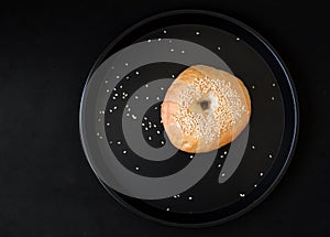 A Single Bagel with Sesame on dark plate