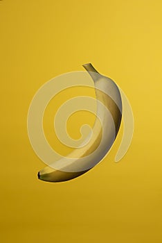 Single banana in peel on yellow background