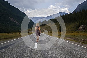 Single barefoot woman is walking along the mountain road. Travel, tourism and people concept