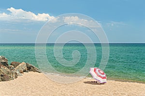 Single beach umbrella on empty beach with rocks