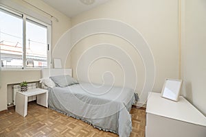 Single bed with blue bedspread with white headboard, matching side table