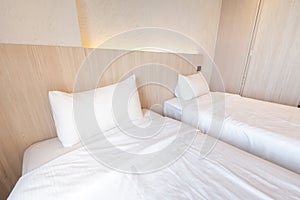 2 single beds with white bedding are in the cream bedroom of hotel that turn on the headboard light and open the gray curtain