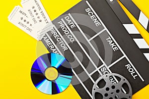 Single, black, open movie clapper or clapper-board with dvd movie disc, film reel and movie theatre tickets flat lay top view from