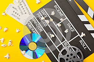 Single, black, open movie clapper or clapper-board with dvd movie disc, film reel, popcorn and movie theatre tickets flat lay top