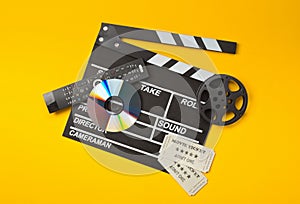 Single, black, open movie clapper or clapper-board with dvd movie disc, film reel, remote control and movie theatre tickets on