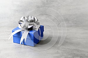Single blue gift box with silver ribbon on gray background