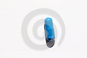 Single blue pill on a white background. Top view, copy space. Hard light, shadow. Medicine capsule on table.