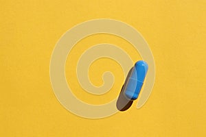 Single blue pill on a yellow paper background. Top view, copy space. Medicine capsule on colored backdrop