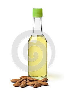 Single bottle with almond oil and a heap of almonds on white background close up