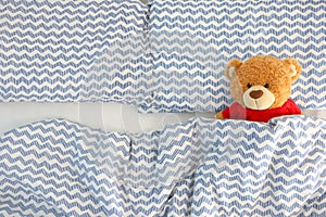 Single brown bear doll wear red shirt sleeping on the bed have space on the left side. Concept waiting for someone to sleep with h