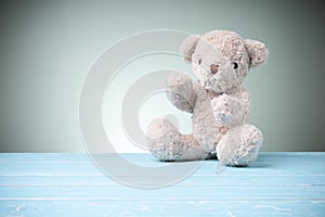 Single brown teddy bear furry setting on a blue wooden table on the green background behind