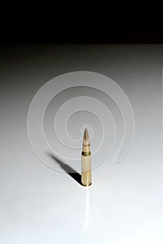 A single bullet 7.62 x 51 mm NATO standing on a white surface with a black background