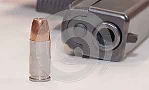 A single bullet on a white table with a black pistol in the background
