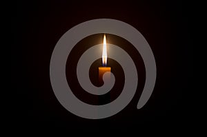 A single burning candle flame or light glowing on a Single small yellow candle is isolated on black or dark background on table in