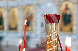 Single candle with dripping wax and blurring lights of many candles in two candlesticks at background