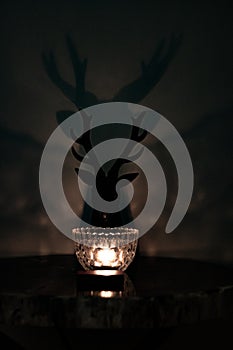 Single candle glowing with silhouette of deer head with antlers outlined against the wall