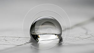 A single clear water droplet rests on a smooth slightly textured surface