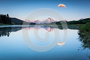 Single cloud in blue sky and reflection in Oxbow Bend lake during sunrise