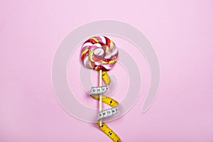 Single colorful lollipop with measuring tape on pink background.