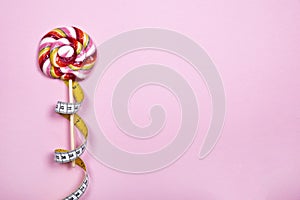 Single colorful lollipop with measuring tape on pink background.