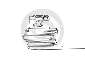 Single continuous line drawing of vintage classic analog pocket camera above stack of books on desk. Old retro photography