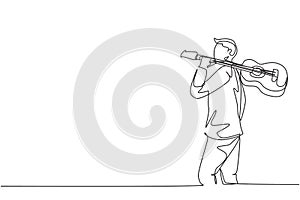 Single continuous line drawing of young happy male guitarist walking while carrying acoustic guitar oh his shoulder. Modern