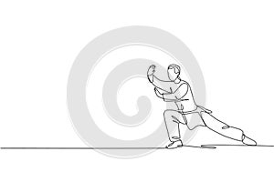 Single continuous line drawing of young man wushu fighter, kung fu master in uniform training tai chi stance at dojo center.