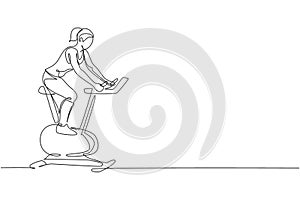 Single continuous line drawing of young sportive woman training with static stationery bike in sport gymnasium club center.