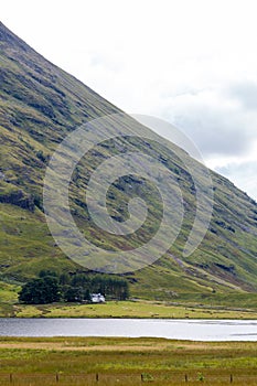 Single cottage in valley at lake and small forest in Scotland