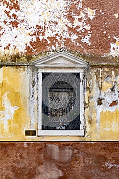 Single crooked window with rusted metal bars on an old semi-destroyed mossy wall in Venice, Italy