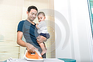 Single dad is ironing while carrying his son. People and Lifestyles concept. photo