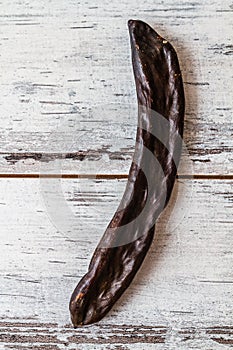 Single Dried Carob Pod on a Textured White Wooden Background