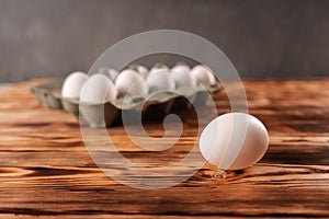 A single egg on the background of a package of eggs on a wooden table