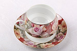 Empty porcelain tea cup with saucer and floral pattern on a table with white tablecloth